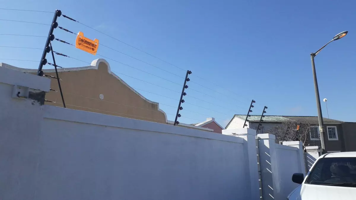 Electric security fence on a white boundary wall against a blue sky