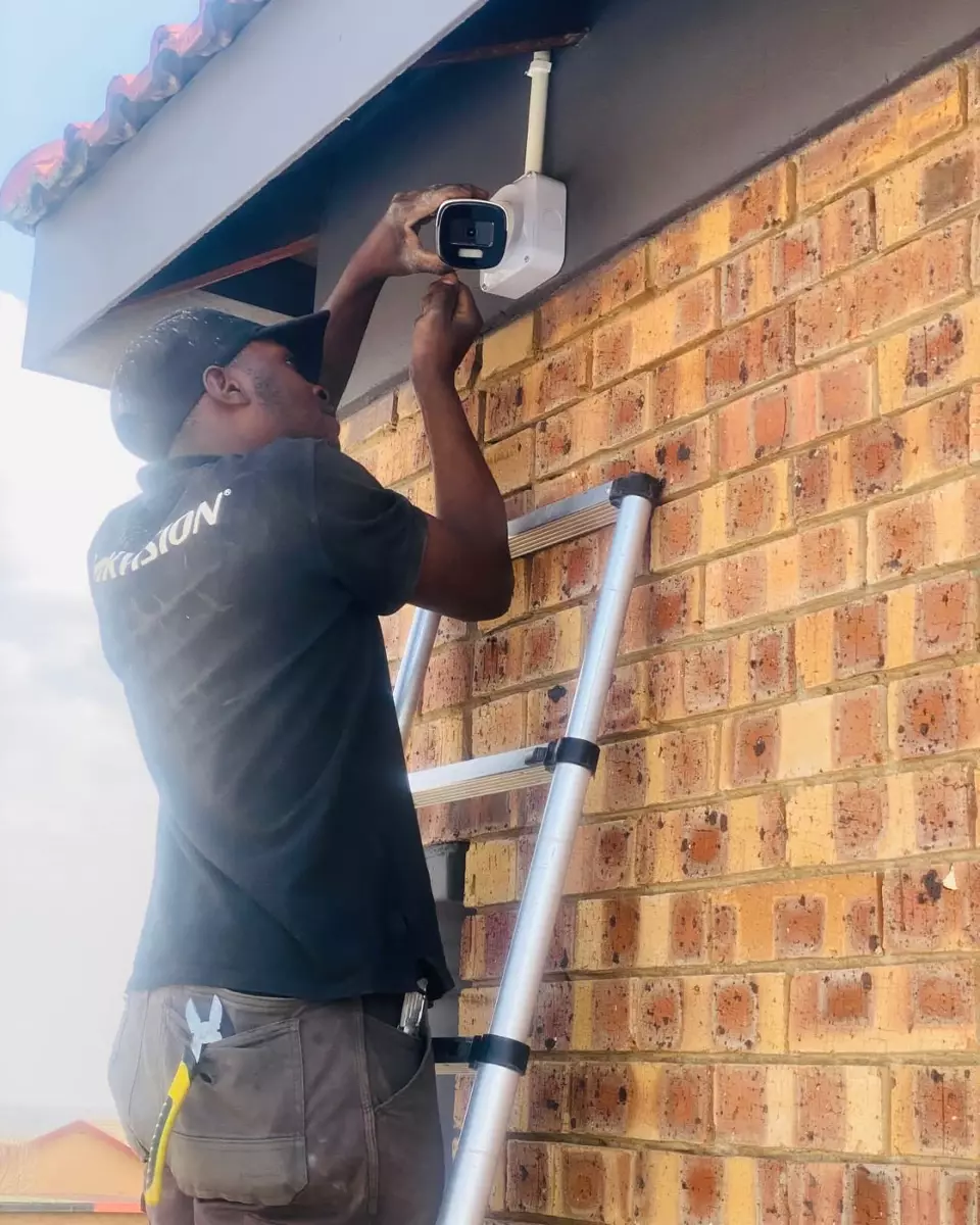 Worker on a ladder mounting a security camera on an exterior brick wall
