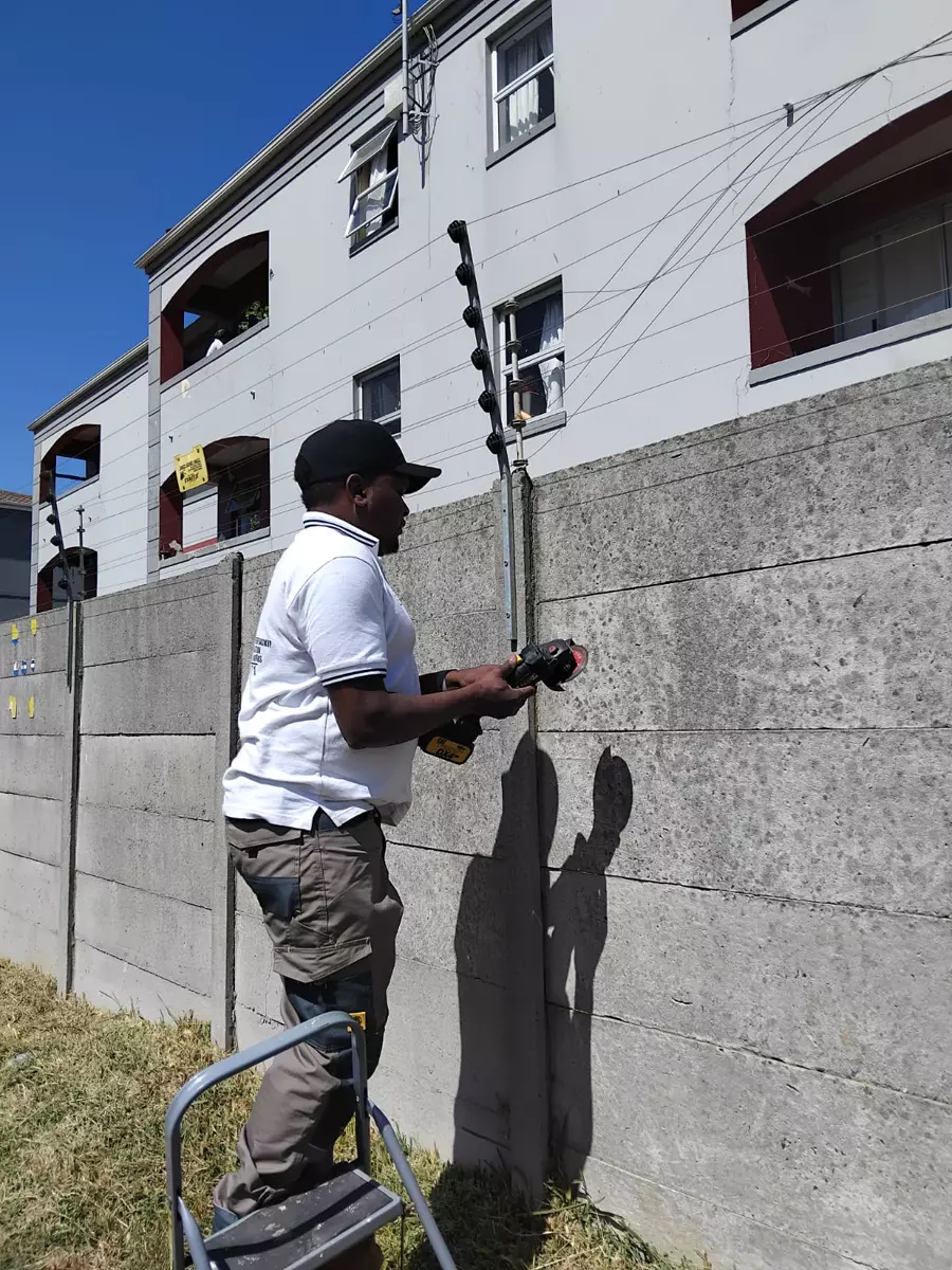 Worker on a stepladder installing an electric fence on a concrete wall