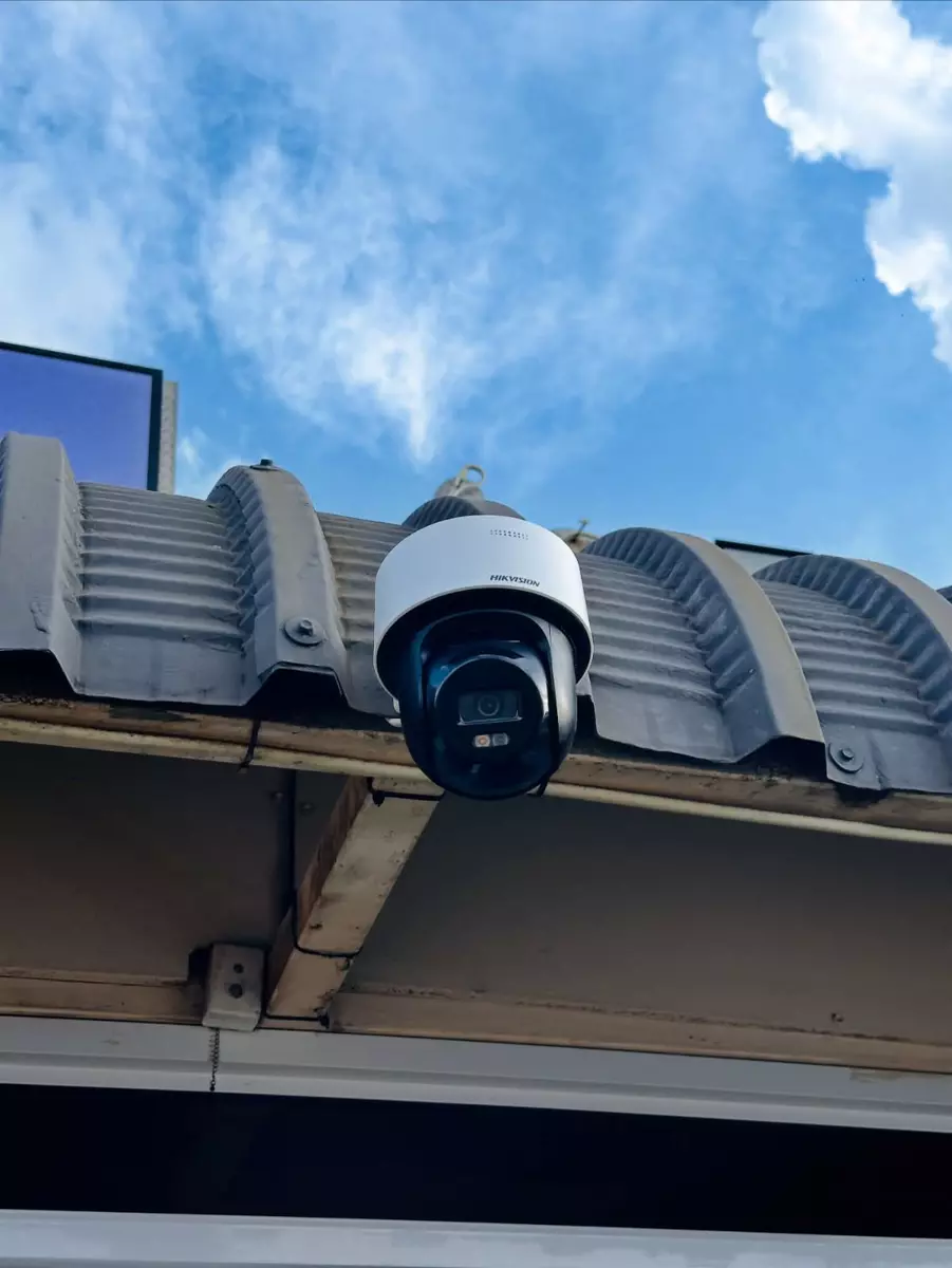 PTZ security camera mounted on a corrugated metal roof against a blue sky