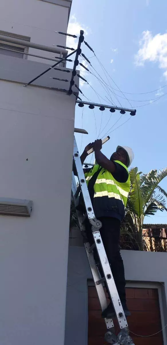Technician on a ladder installing electric fencing on a building wall