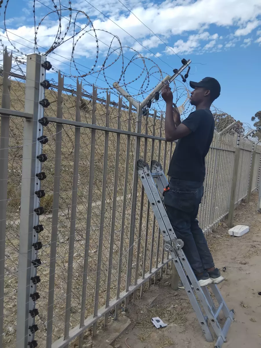 Worker on a ladder installing security and electric fencing