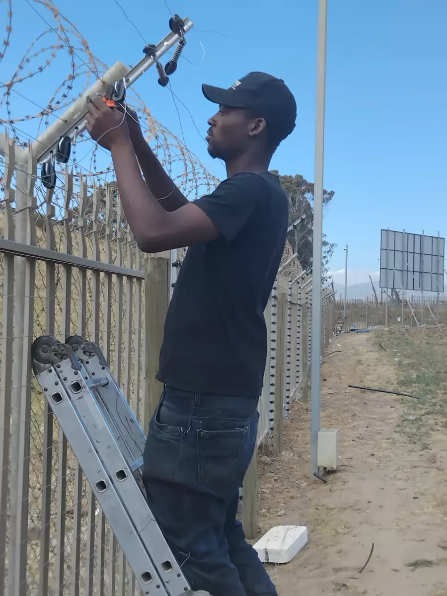 Technician on a ladder repairing a security and razor wire fence